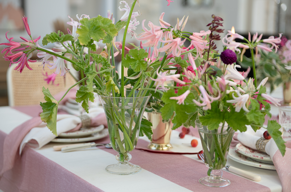 Clear glass footed vases with pink and green flower arrangements on pink stripe linens