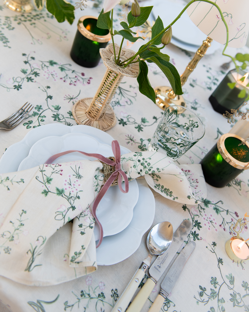 Dinner table setting on botanica linen tablecloth and napkin with rattan napkin ring with pink velvet bow, rattan petal bud vase and scented candles