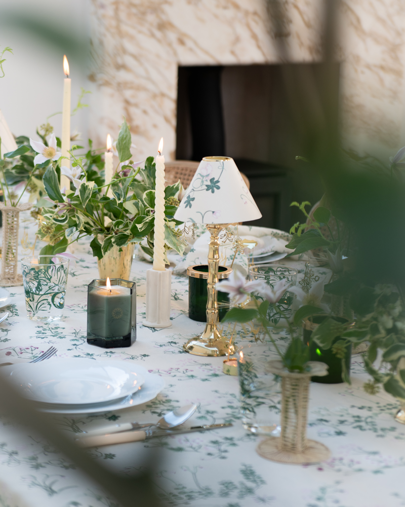 Botanica dinner table setting with tealight candle stands with shades, scented candles, rattan petal bud vases and green and cream flower arrangements