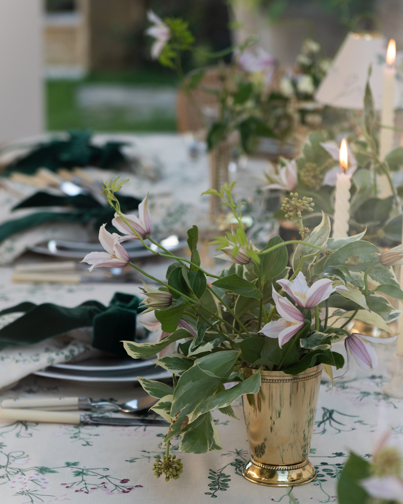 Brass julep cup vase with green and pink floral arrangement on a botanica linen dinner table setting with green velvet bows