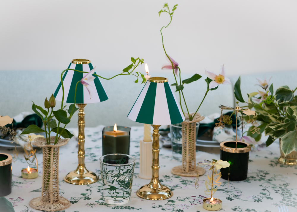 Green and white striped candle shades on brass tealight stands, rattan petal bud vase duo with pink flowers and candles with carousels on botanica linen tablecloth