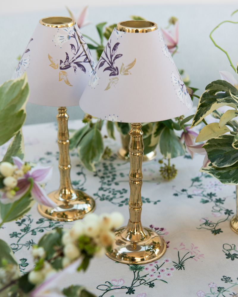 Two maharani candle shades on brass bamboo style tealight stands surrounded by green flower arrangements on botanica linen tablecloth