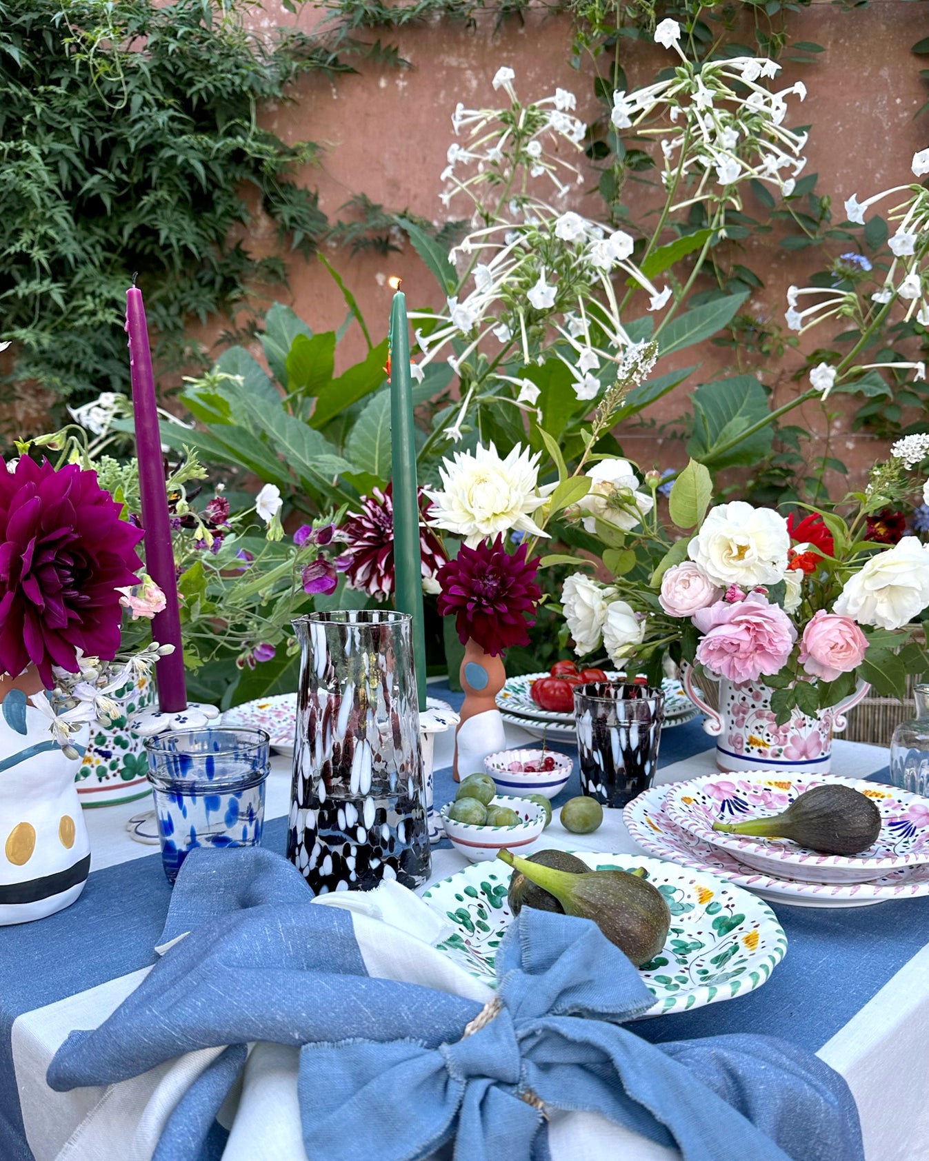 Decorative outdoor table setting with flowers, striped linen napkins, candles, and colorful plates.