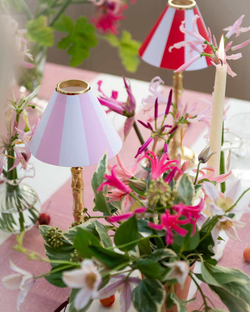 Pink and green floral arrangements and brass tealight stands on a pink stripe linen tablecloth with pink and red stripe candle shades