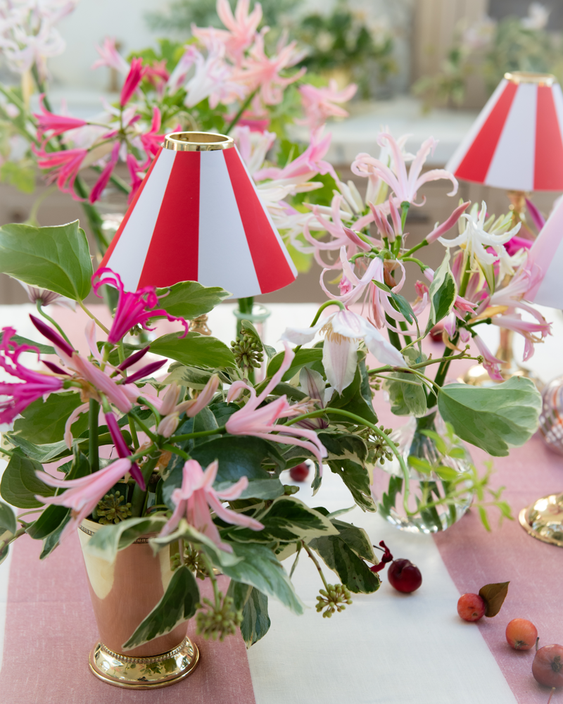 Decorative table setting with pink flowers, green leaves, and red and white striped lampshades.