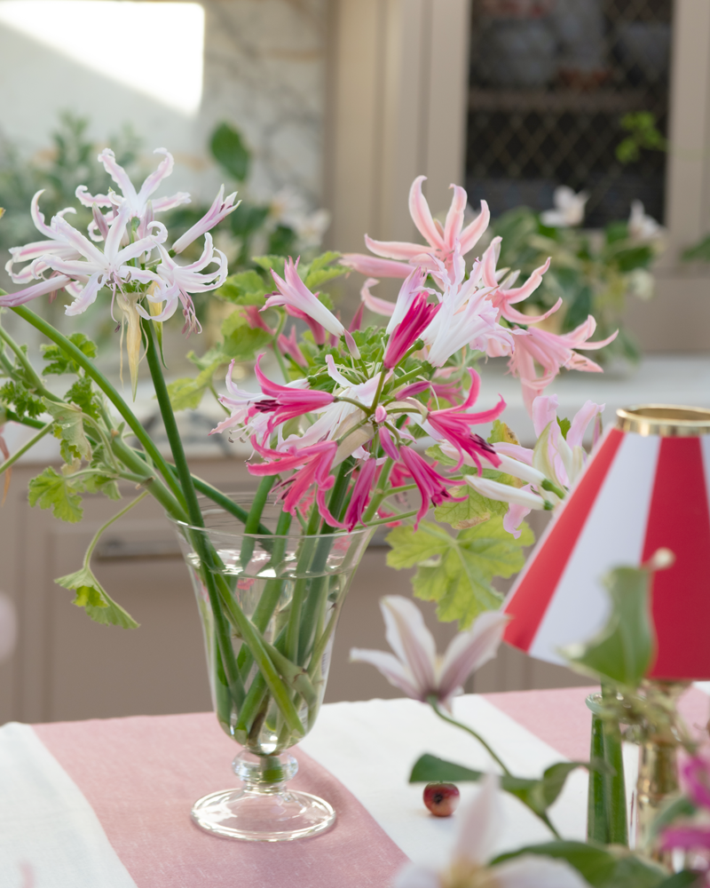 Clear glass footed vase with pink white and green flower arrangement on a pink stripe linen tablecloth