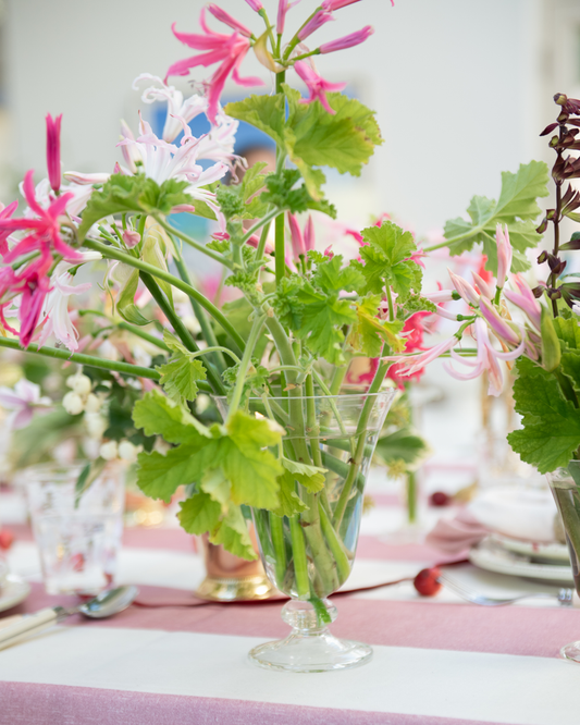 Clear glass footed vase with pink and green flower arrangement on a pink stripe linen tablecloth
