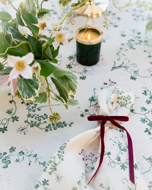 Botanica linen tablecloth and napkin with rattan napkin ring and red velvet bow, scented candle with carousel and floral arrangement