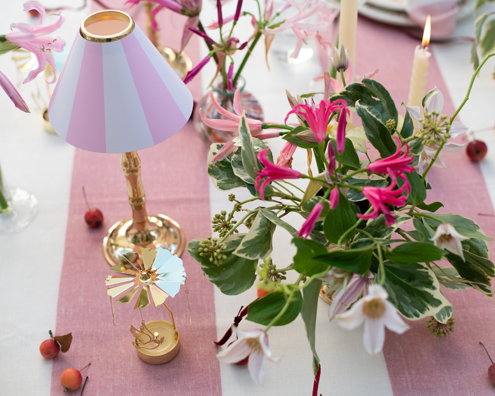Dove tealight carousel with pink and green floral arrangement and brass tealight stand with pink and white striped candle shade on pink stripe linen tablecloth