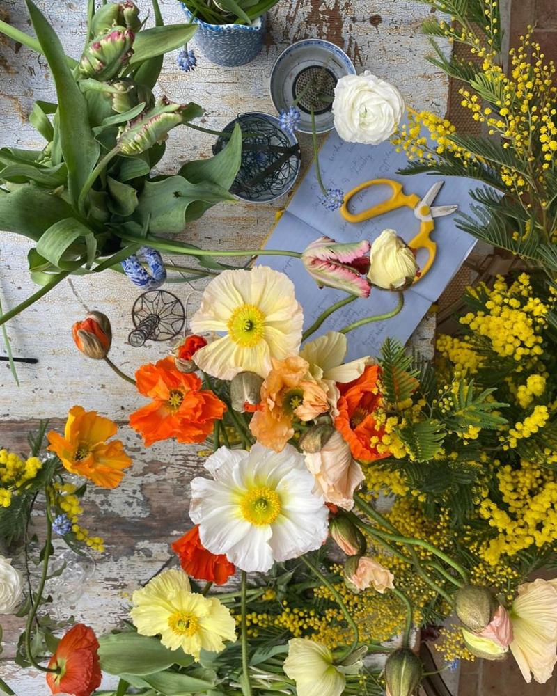 Floral arrangement on a wooden table with scissors, notebook, kenzan pin holder and flowers.